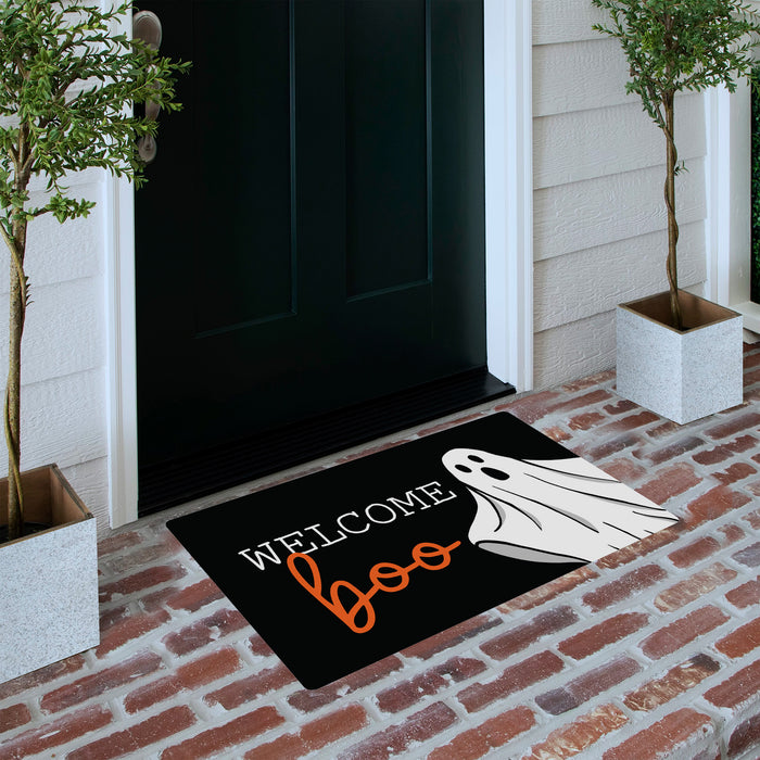 A black Halloween doormat with the words 'Welcome Boo' and a white ghost graphic, placed on a brick porch in front of a dark door with potted trees on either side.