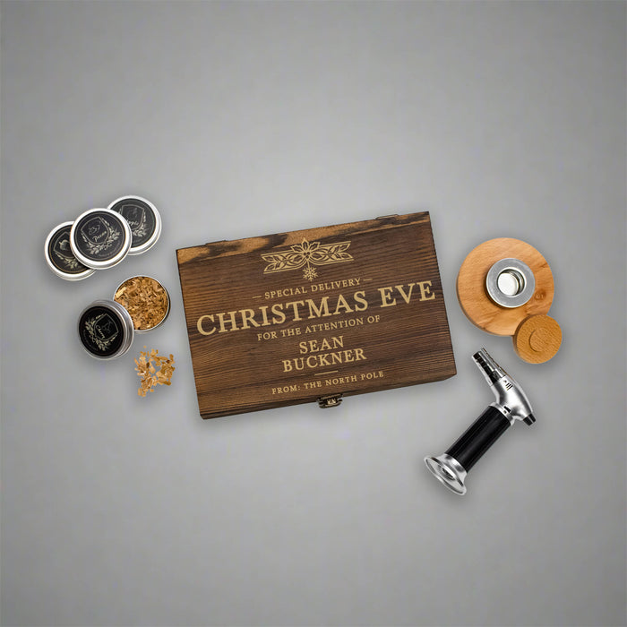 A personalized Christmas gift whiskey smoker set arranged on a neutral gray background, featuring a wooden box engraved with 'CHRISTMAS EVE' and 'SEAN BUCKNER'
