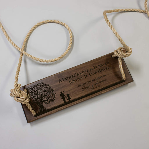 Wooden tree swing with engraved text and tree design, hanging from rope on a light gray background