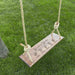 Wooden swing with engraved text on a grassy background