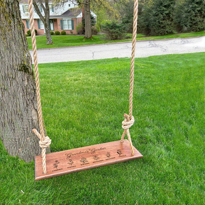 Wooden swing with engraved text hanging from a tree in a grassy area with a house across the street