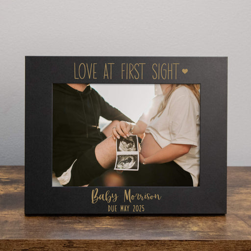 Black photo frame with 'Love at First Sight' text, holding a couple with ultrasound images.