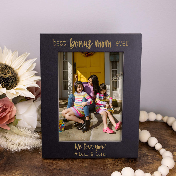 Black photo frame with 'best bonus mom ever' text, featuring a family photo on a wooden surface.