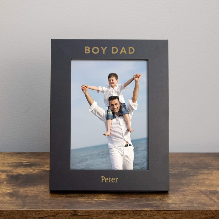 Black photo frame with a picture of a man and a boy on a wooden surface and gray background.
