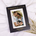 Black picture frame with "Promoted to Grandma" engraved in light brown on a white background next to white floral