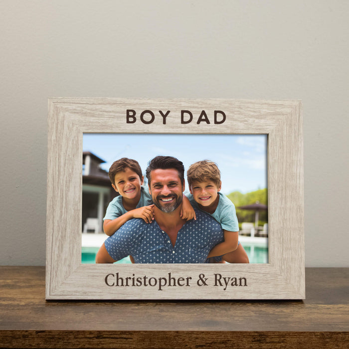 Wooden photo frame with 'BOY DAD' text and a family photo inside, on a wooden surface.