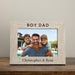 Wooden photo frame with 'BOY DAD' text and a family photo inside, on a wooden surface.