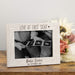 White wooden photo frame with 'Love at First Sight' text, holding ultrasound images of a baby, on a wooden surface with flowers.