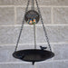 Black metal bird bath with decorative plaque against a brick wall.