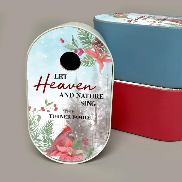 Personalized white Christmas-themed bird house in front of blue and red bird house options. The sign features a winter forest scene with a cardinal, poinsettias, pinecones, and the text 'LET Heaven AND NATURE SING THE TURNER FAMILY.