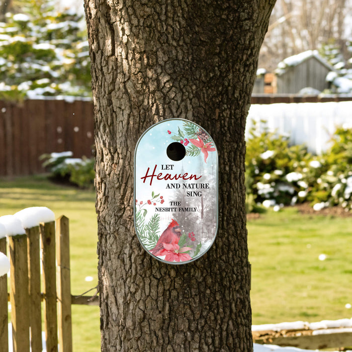A personalized blue bird house with a winter theme, featuring a red cardinal, red poinsettias, and the text 'LET Heaven AND NATURE SING. THE NISBEE FAMILY' printed on a light blue background, shown hanging on a tree in a snowy backyard.