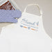 White apron with 'loved beyond measure' text and kitchen utensils, paired with a blue and white striped oven mitt on top of a tray of brownies