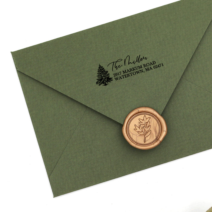 An olive green paper envelope sealed with a round copper-toned wax seal, featuring a black printed address and Christmas tree on the flap, shown on a white background.