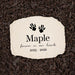Personalized pet memorial garden stone with black hamster paw prints, the name 'Maple', and the years '2023 - 2026' on a light beige stone, placed on a bed of dark brown mulch.