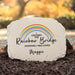 Personalized memorial garden stone with a printed rainbow and the text 'I Crossed the Rainbow Bridge Knowing I Was Loved Maggie' set in mulch outdoors.