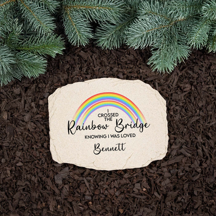 personalized pet memorial grave marker printed with a rainbow design and saying resting on mulch next to a pine tree