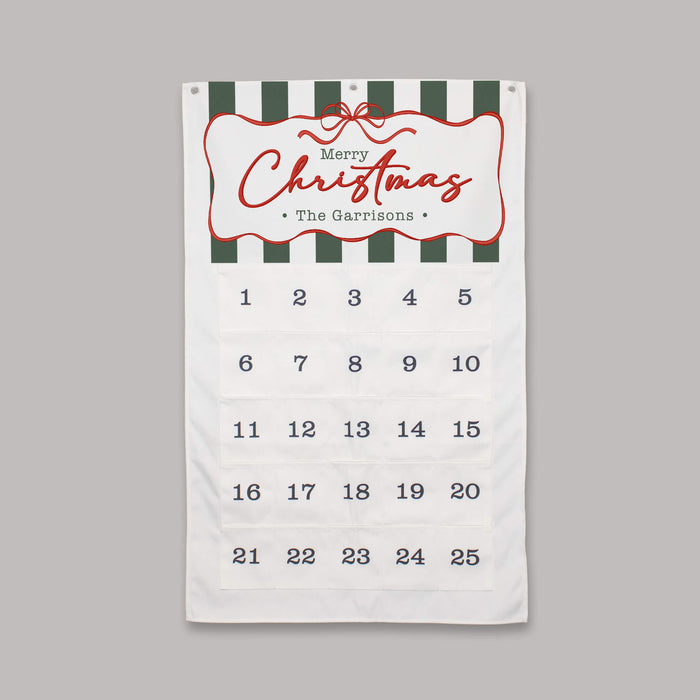 A personalized Christmas advent calendar featuring a white fabric body with dark green and white striped accents at the top, a red decorative border around the 'Merry Christmas The Garrisons' greeting, and 25 numbered pockets for the days of the week on a solid gray background.