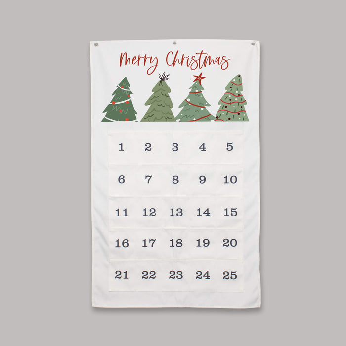 A white Christmas advent calendar with 'Merry Christmas' written in red script at the top, decorated with four green Christmas trees. Below the greeting is a grid of 25 numbered pockets for the days of the week, spanning the 25 days of Christmas.