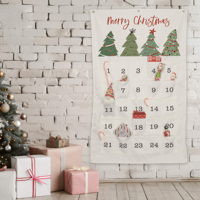A Christmas advent calendar hanging on a white brick wall, with wrapped gift boxes and a decorated tree beside it. The calendar has numbered pockets and festive illustrations including Christmas trees and is filled with candy canes and gifts.