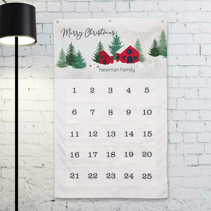 A personalized Christmas advent calendar for the 'Newman Family' hanging on a white brick wall. The calendar features a festive winter illustration at the top with 'Merry Christmas' and the family name, followed by 25 numbered pockets.
