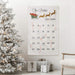 A personalized Christmas advent calendar hanging on a white wall in a decorated living room, next to a flocked Christmas tree and wrapped gifts.