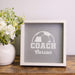 Framed sign with 'COACH Carson' text and soccer ball design on a wooden surface with flowers.