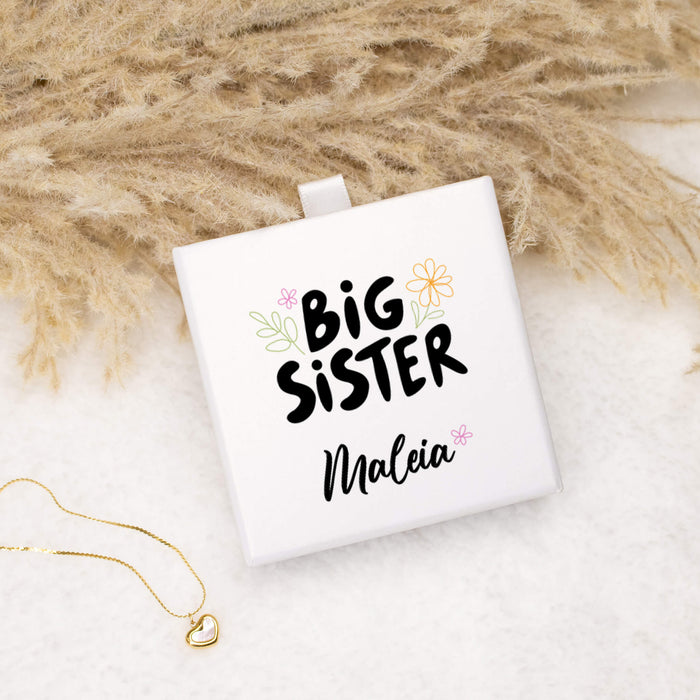 White square box with 'Big Sister' text on a textured surface with pampas grass.