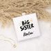 White square box with 'Big Sister' text on a textured surface with pampas grass.