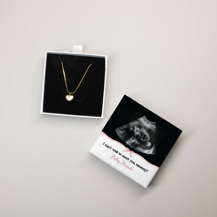 Gold heart necklace in a box with an ultrasound photo and message on a light gray background