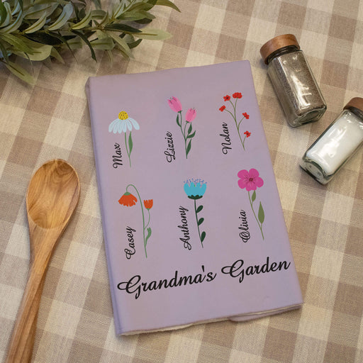Purple towel with floral designs and names on a checkered tablecloth with a wooden spoon and salt and pepper shakers.