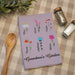 Purple towel with floral designs and names on a checkered tablecloth with a wooden spoon and salt and pepper shakers.