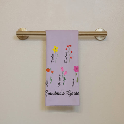 Floral-themed towel that says "Grandma's Garden" with names on a towel rack against a beige wall