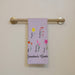 Floral-themed towel that says "Grandma's Garden" with names on a towel rack against a beige wall