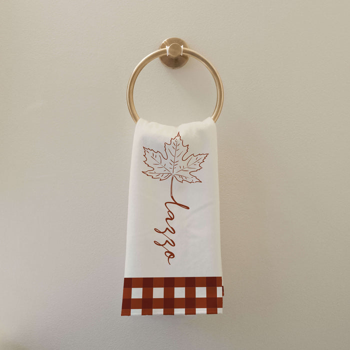 autumn bathroom towel printed with a maple leaf, custom last name, and rust colored gingham hanging on a gold towel loop