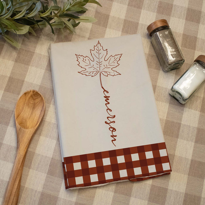 fall design towel printed with a custom last name on a plaid tablecloth next to kitchen items