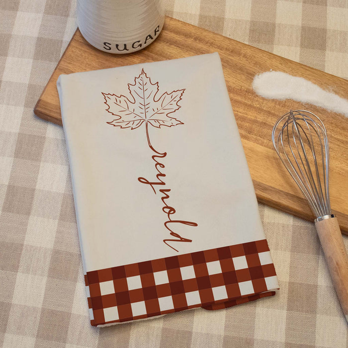 autumn designed kitchen towel on a wooden cutting board next to a jar of sugar and a whisk
