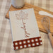 autumn designed kitchen towel on a wooden cutting board next to a jar of sugar and a whisk