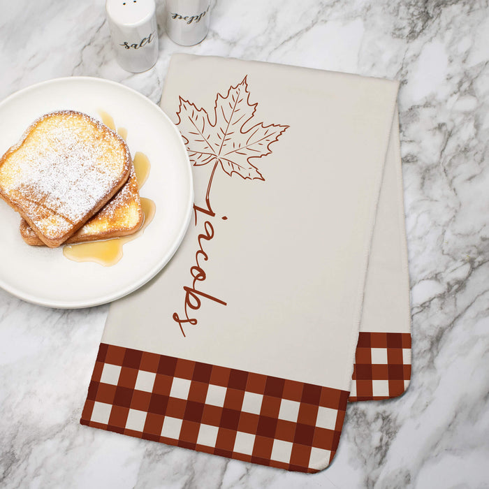 Fall maple leaf designed towel printed with a custom last name on a marble countertop next to a plate of french toast with syrup