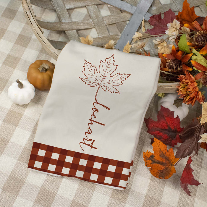 custom last name towel designed with a maple leaf and gingham on a plaid tablecloth next to fall florals