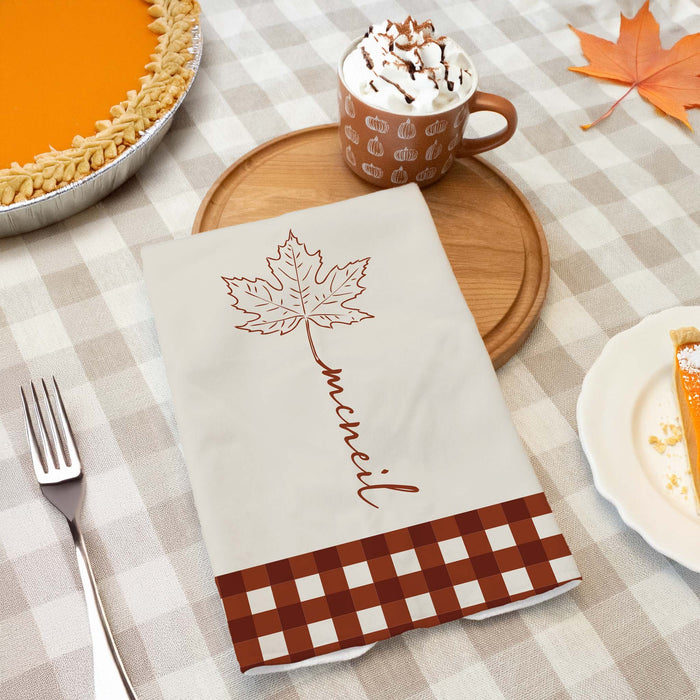 autumn leaf kitchen towel personalized with a custom last name on a Thanksgiving dinner table next to a pumpkin pie and hot chocolate