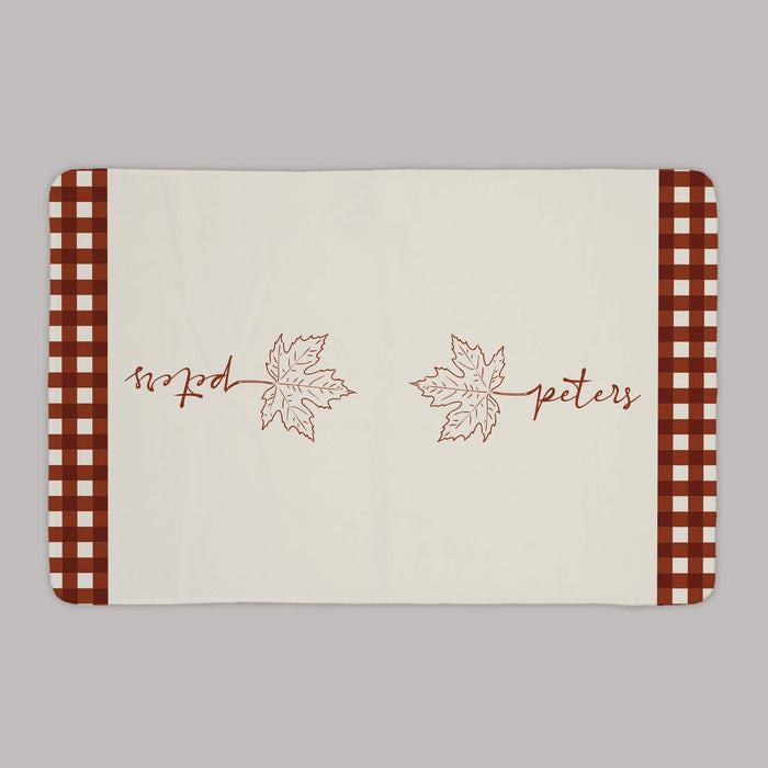 Thanksgiving kitchen towel designed with a maple leaf, custom name, and rust colored gingham on a gray background