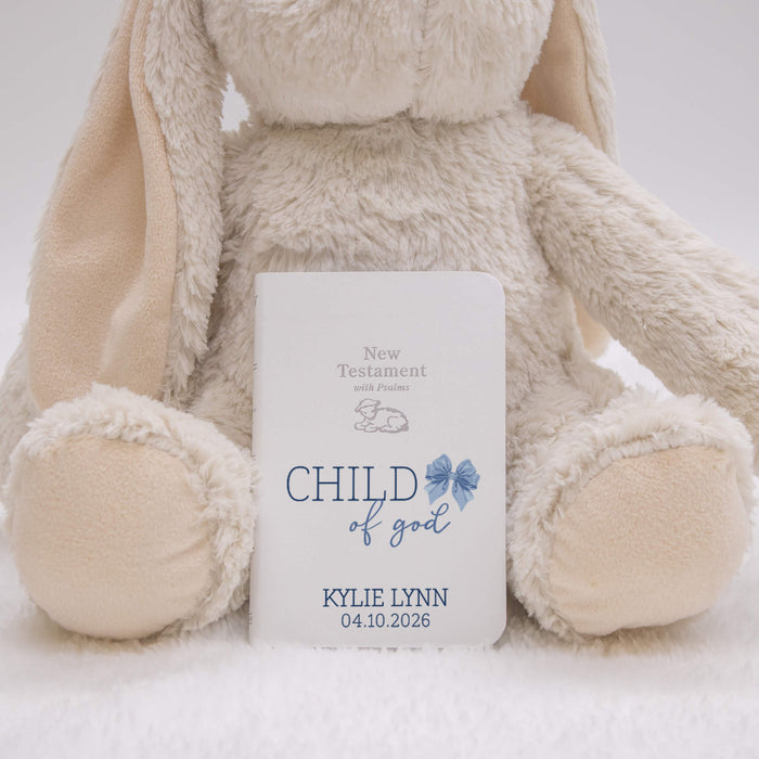 Fluffy beige bunny behind a baby bible labeled 'Child of God' with a blue bow design