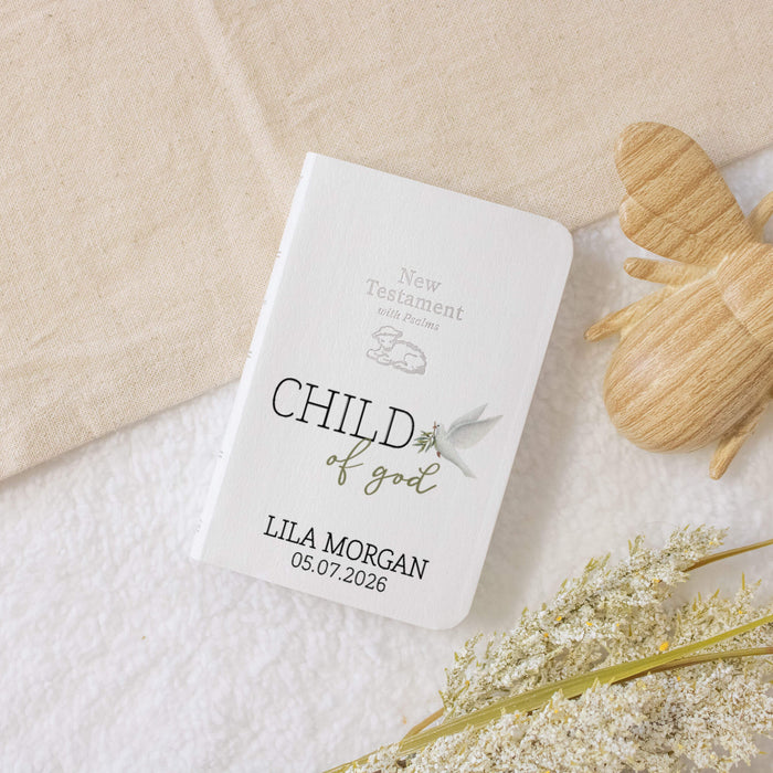 Personalized baby bible with 'Child of God' inscription on a textured surface with flowers and wooden bee.