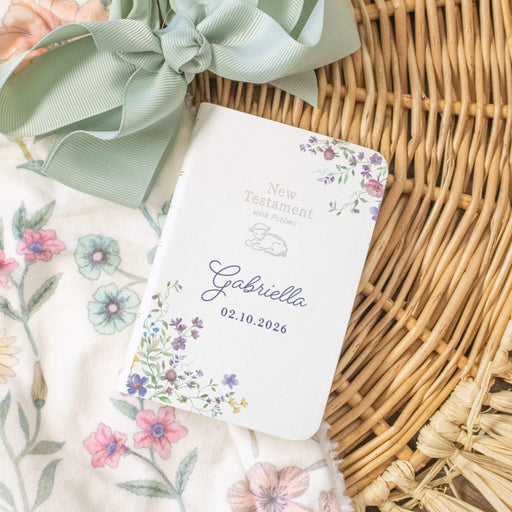 Personalized New Testament with floral design and light blue ribbon on wicker surface