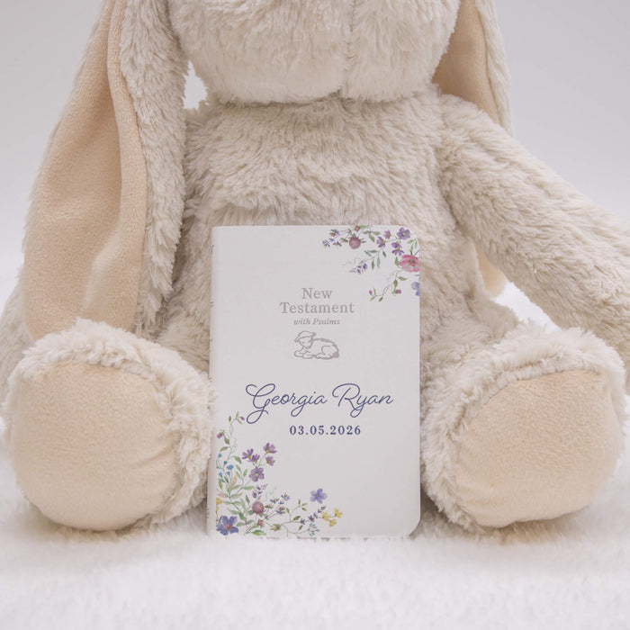Floral New Testament with personalized name and date, held by a plush bunny toy on a white background