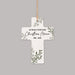 A white cross-shaped memorial ornament with green leaf illustrations and black personalized text reading 'AT PEACE WITH GOD Christian Moore 1981 - 2025', hanging from a natural jute string against a solid gray background.
