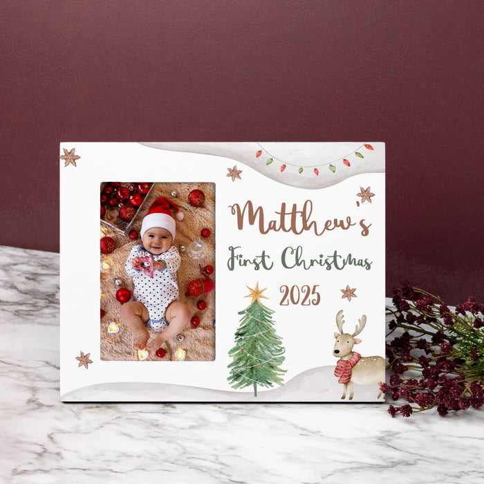Christmas-themed picture frame for 'Baby's First Christmas 2025' with a baby photo, trees, and deer on a marble surface.