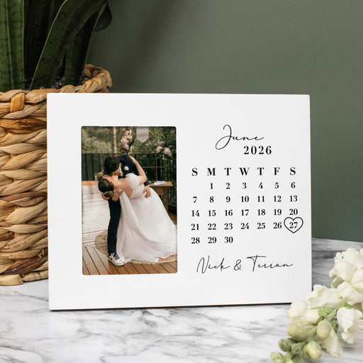 Calendar picture frame with a photo of a couple on their wedding day, against a green wall with decorative elements.