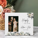 Personalized photo frame with floral design and text, placed on a surface with flowers in the background.