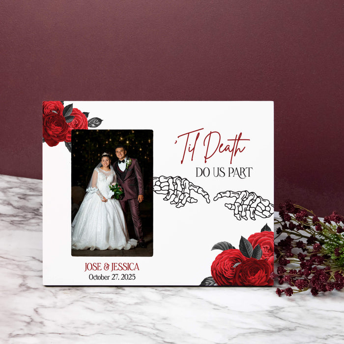 A personalized white photo frame styled on a white marble surface against a dark burgundy background. The plaque features red roses, skeleton hands, and the text 'Til Death Do Us Part' along with a custom wedding photo of a bride and groom.